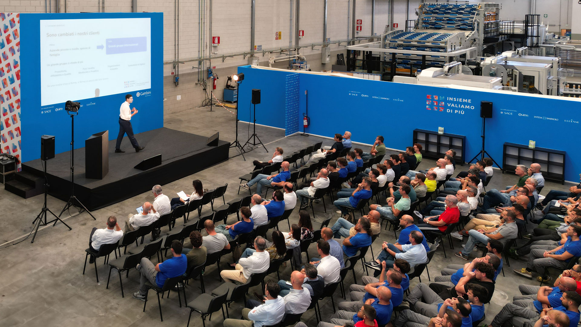 Vista dall'alto della prima Convention aziendale Gambini: un relatore sul palco davanti alla platea, con le linee di produzione sullo sfondo